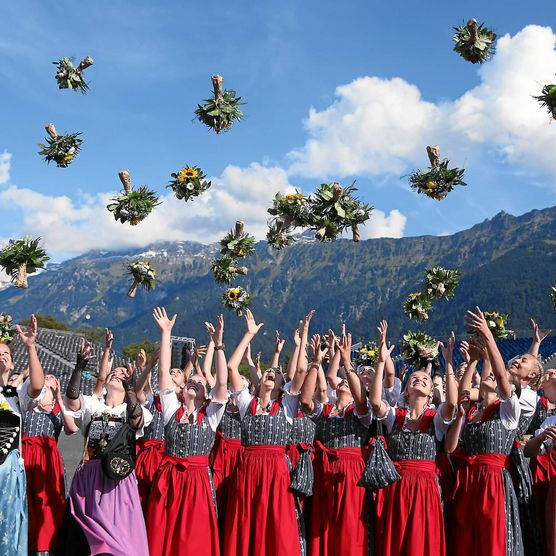 Die in Tracht gekleideten Ehrendamen des Unspunnenfests werfen Blumensträusse in die Höhe. 